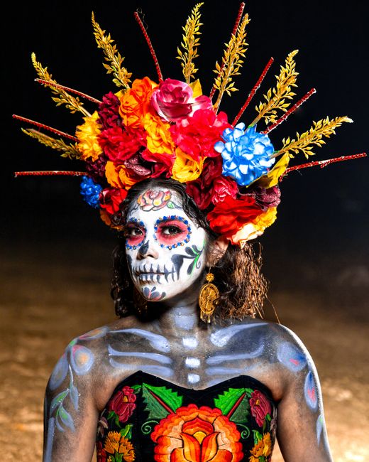 A vibrant Catrina figure with floral makeup and headdress celebrating Día de Muertos at night.