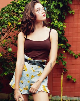 一位戴着眼镜、身穿花卉裙子的时尚年轻女子，在户外倚着红墙摆姿势