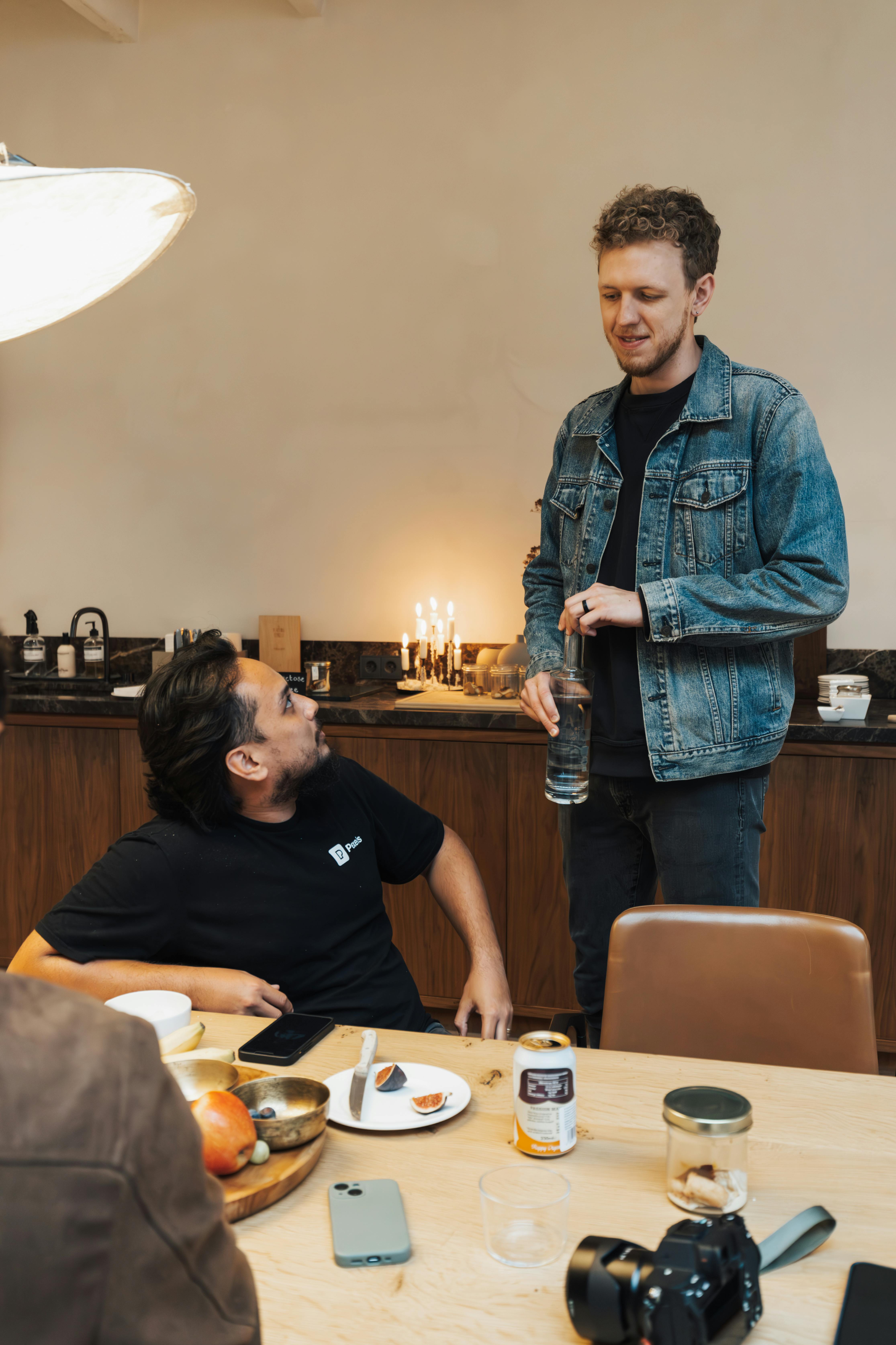 Two friends interacting warmly in a cozy kitchen space with food and drinks.