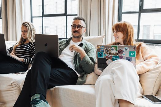 Three adults working on laptops in a casual office environment, discussing ideas.