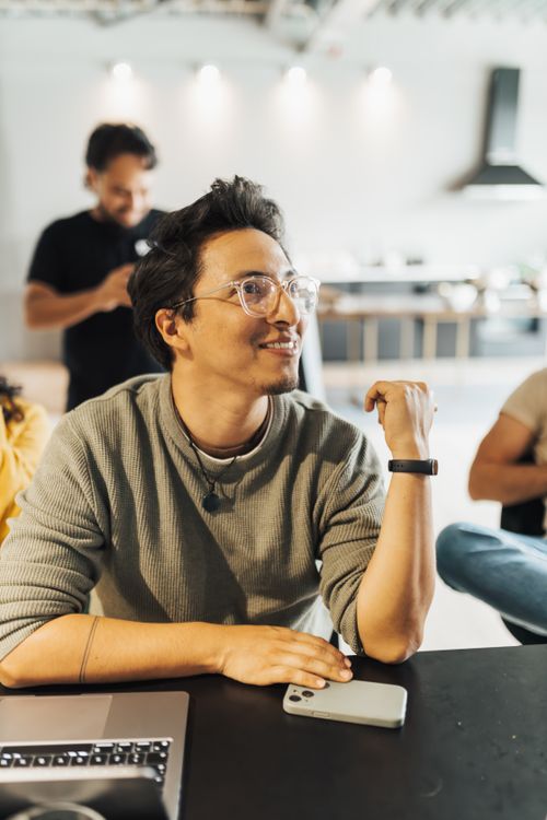 Free Team members engaging in a casual meeting, utilizing smartphones and laptops in a modern office setting. Stock Photo