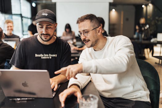 Two men discuss a project on a laptop in a contemporary office setting.