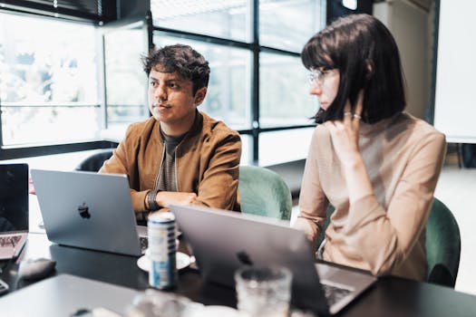 Young professionals collaborate on laptops in a bright, modern office space.