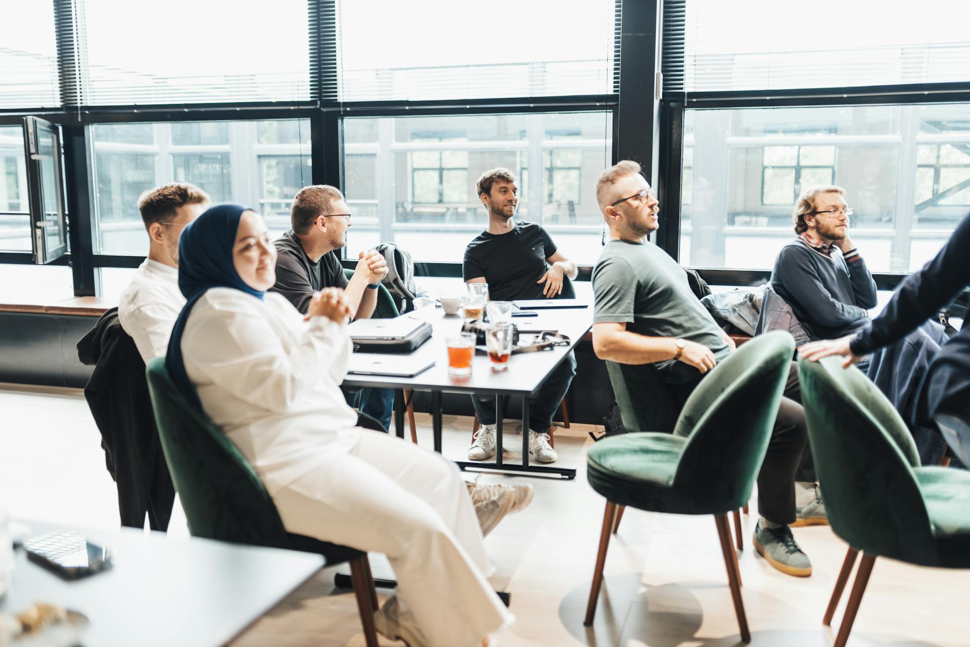 Modern office setting with diverse team in discussion, seated around a table by large windows.