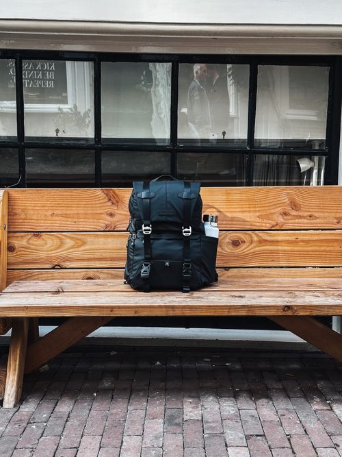 Free A stylish, rugged backpack sits on a wooden bench outside an urban building in Amsterdam. Stock Photo
