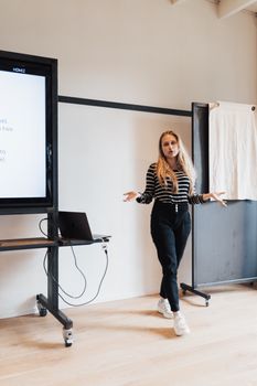 Woman presenting in a modern office with a laptop and screen.