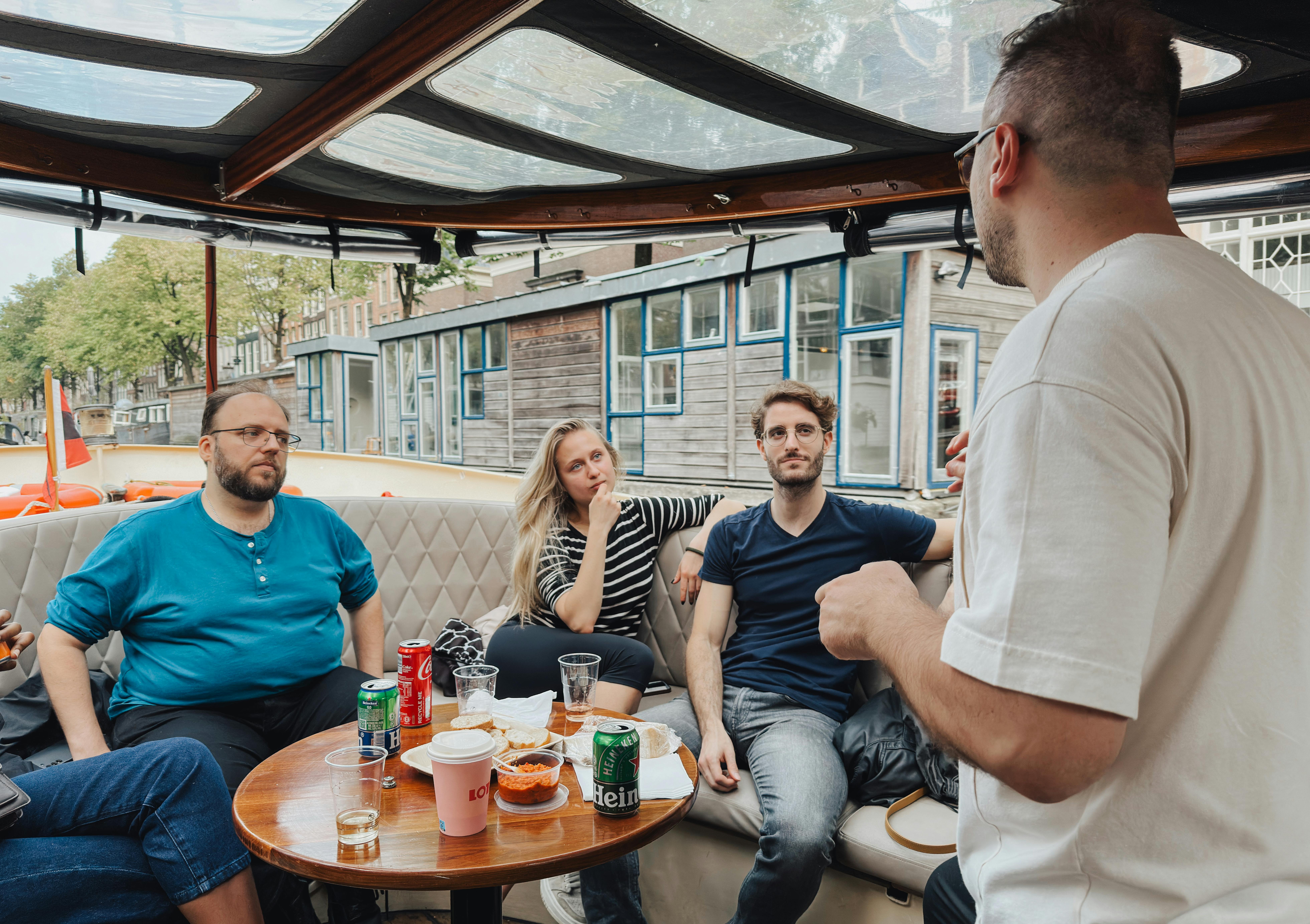 Hollanda'nın ikonik mimarisi eşliğinde bir kanal kenarında veya kafede oturan, neşeyle sohbet eden ve sosyalleşen çok kültürlü bir grup arkadaş.