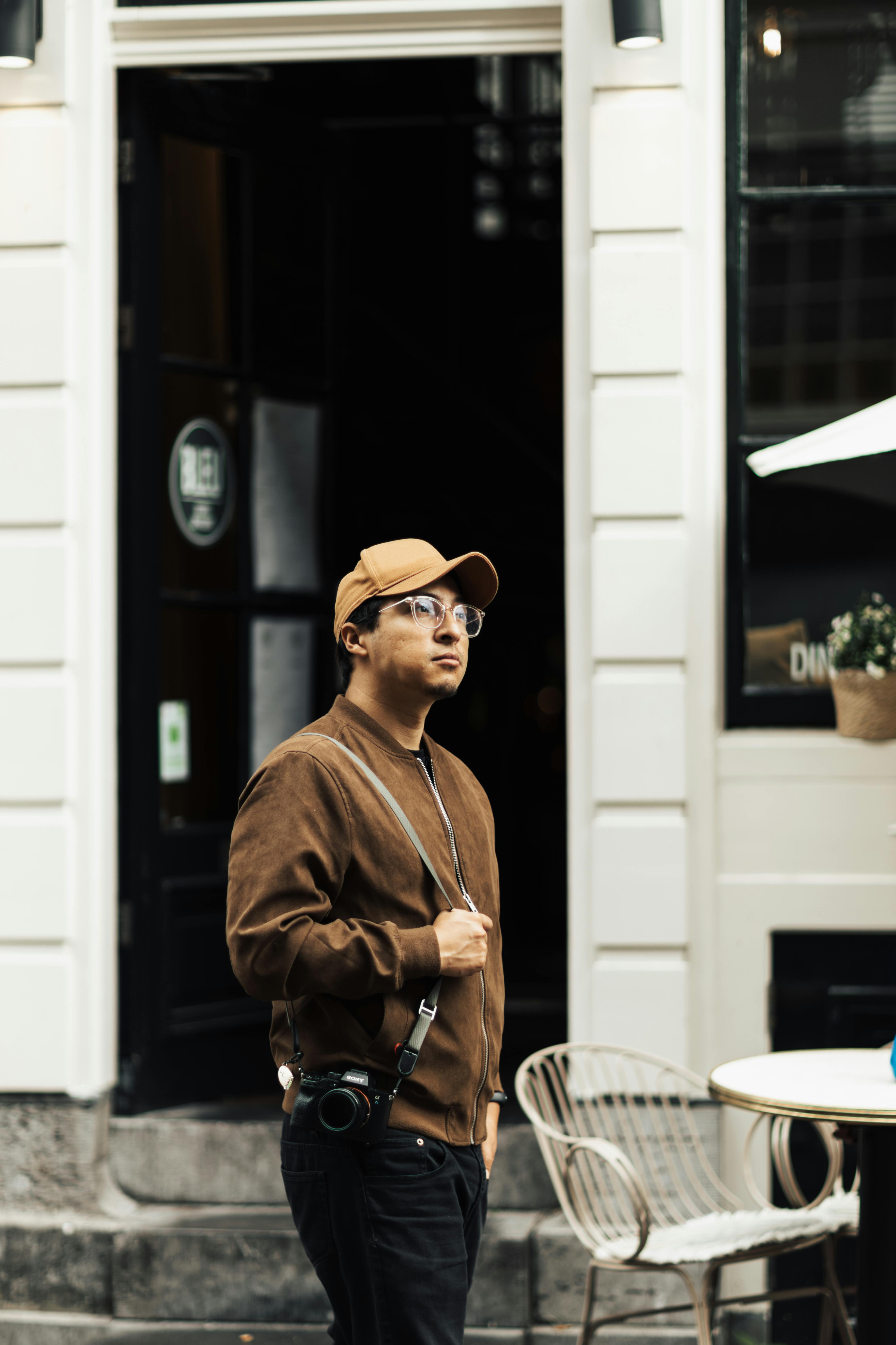 A man wearing a cap and eyeglasses explores city streets with a camera, capturing urban life.