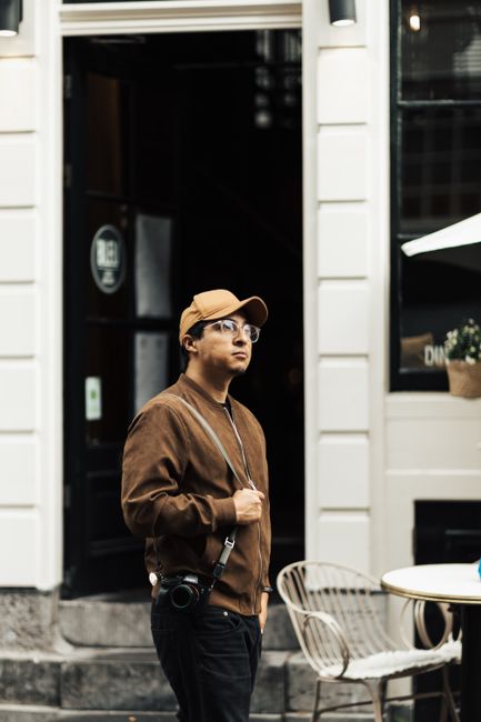 A man wearing a cap and eyeglasses explores city streets with a camera, capturing urban life.