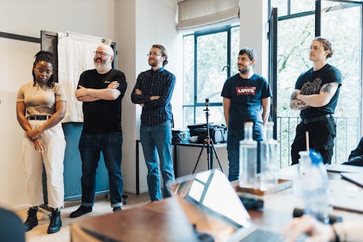 Diverse group of adults in a modern office setting, standing by windows during a casual meeting.