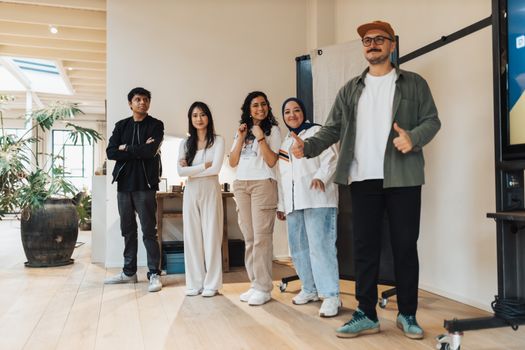 A group of five diverse professionals standing together, smiling indoors.