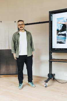 Smiling man giving a presentation in an office with a large display screen.