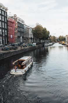 Scenic view of a tourist boat navigating the charming canals of Amsterdam with iconic townhouses lining the water.