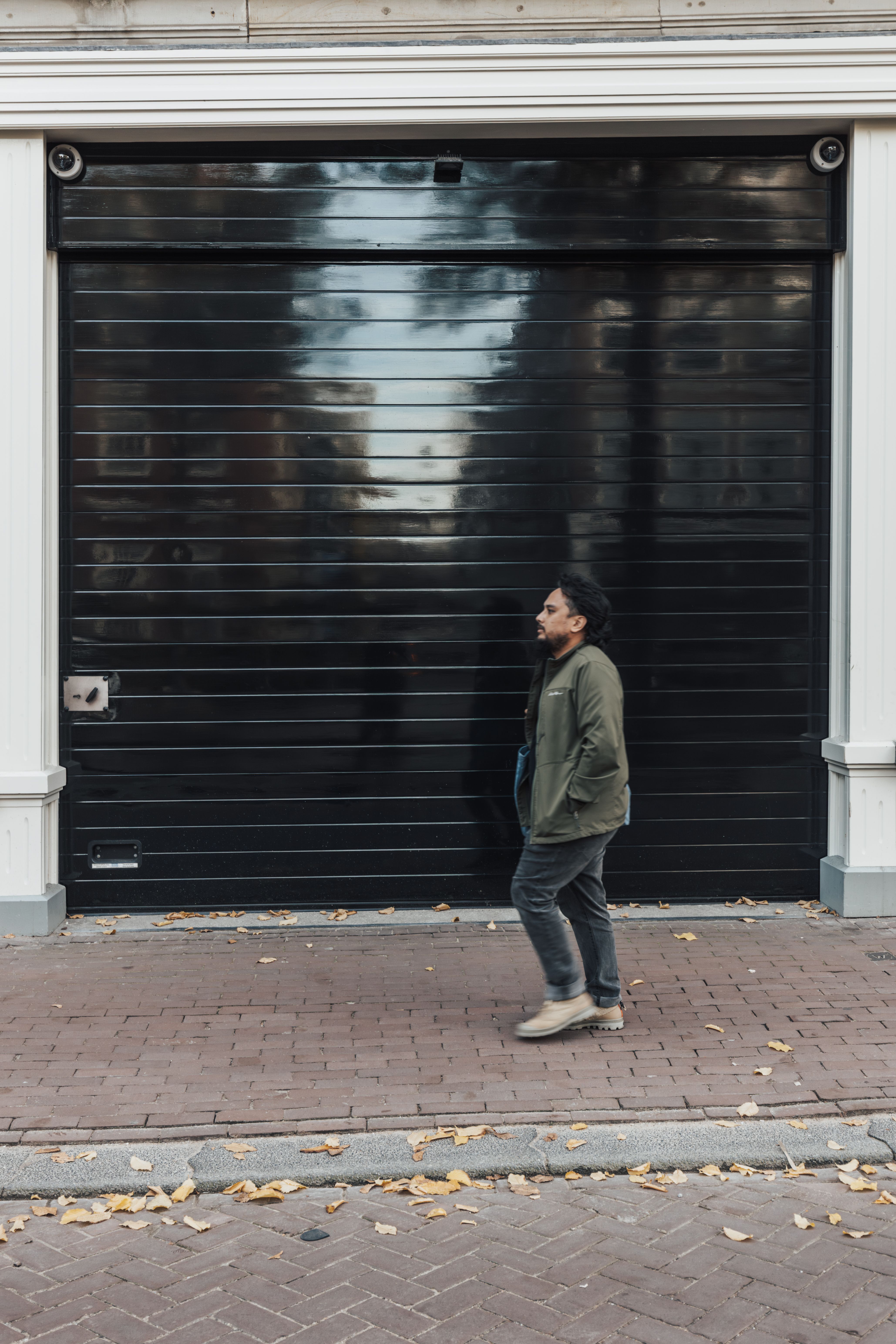 Casually dressed man walks past black garage door in urban setting.
