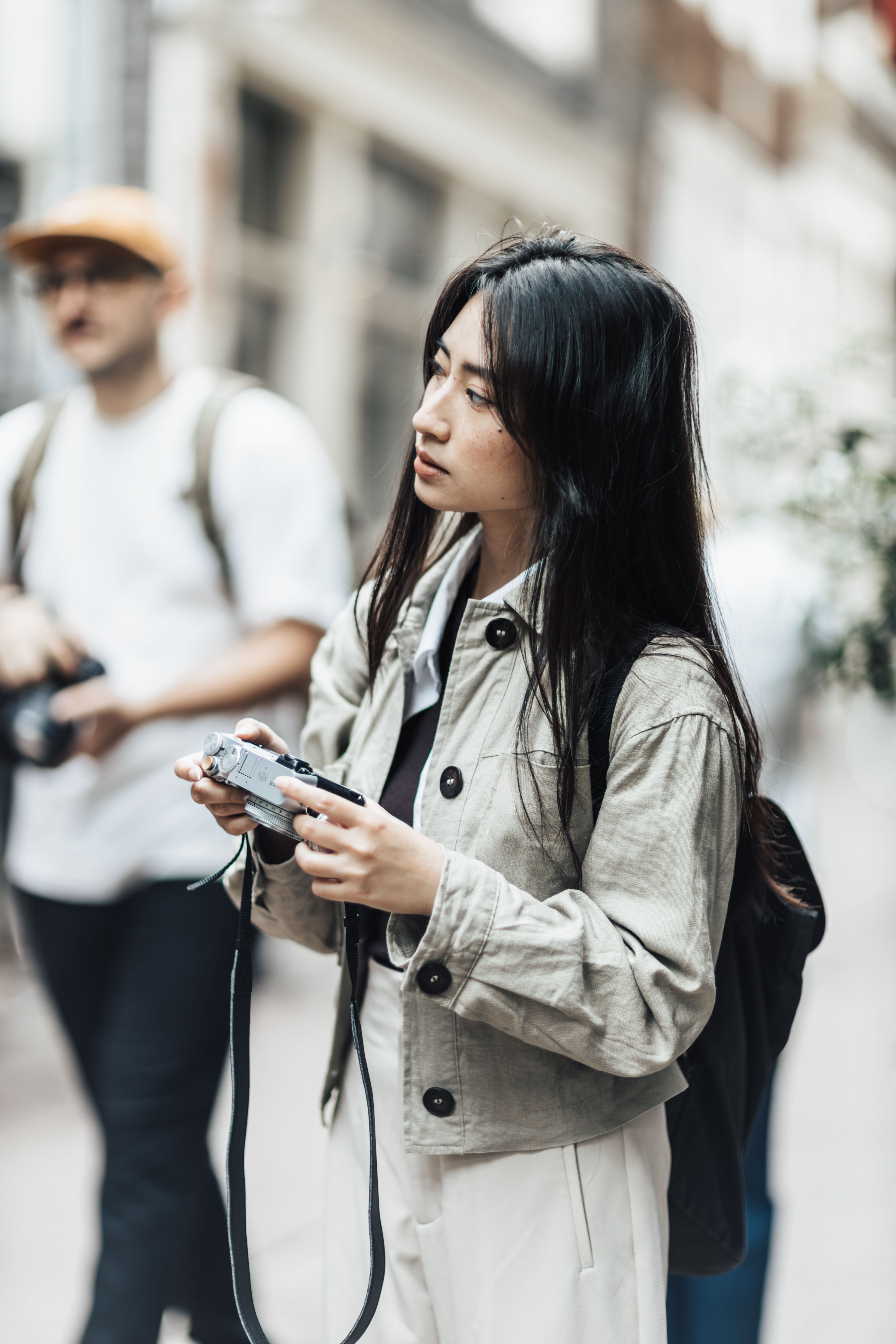 Stylish young woman holding a camera while exploring an urban street, capturing candid moments.