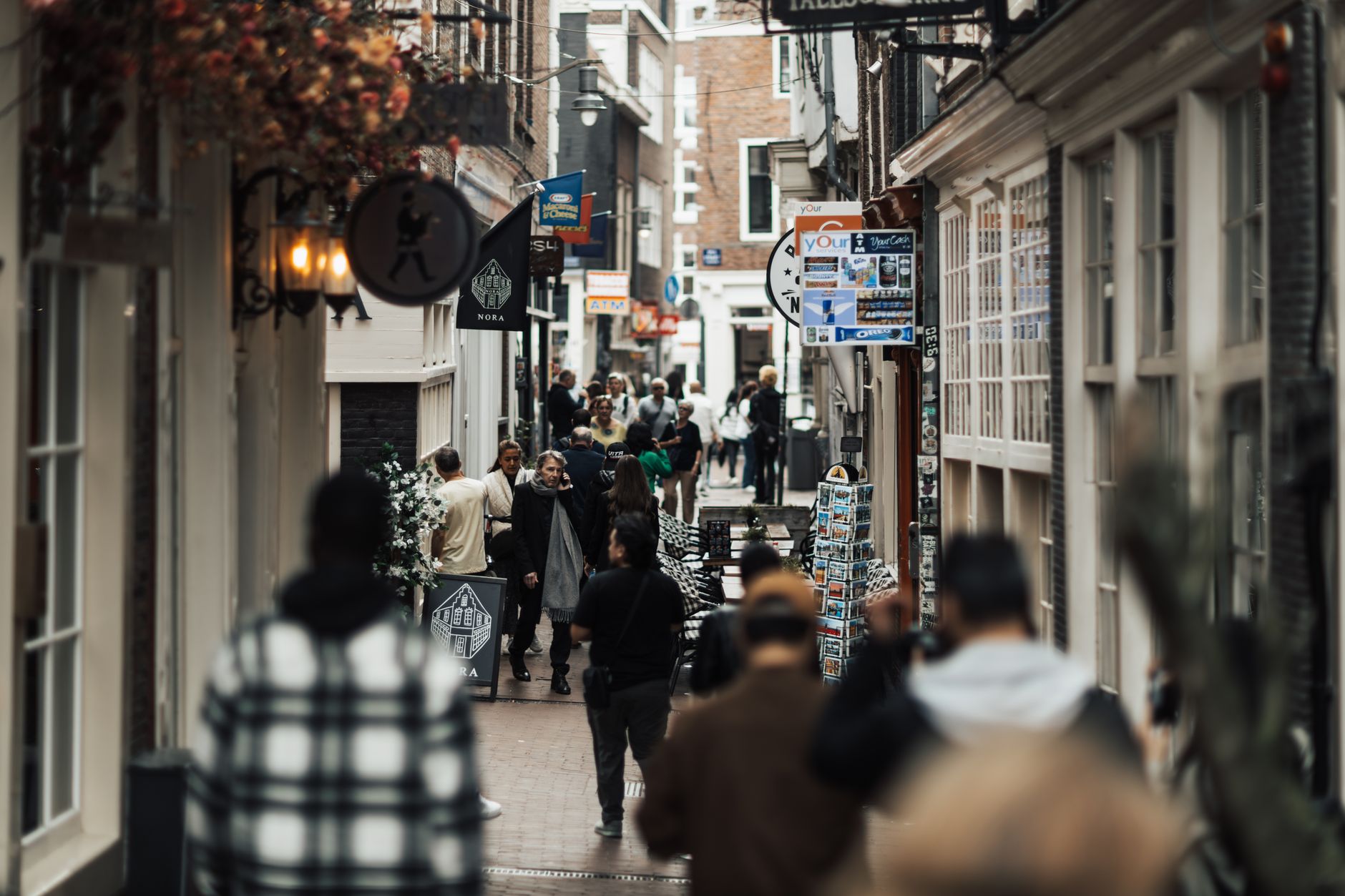 People walking through a narrow urban alley with shops and signs on both sides.