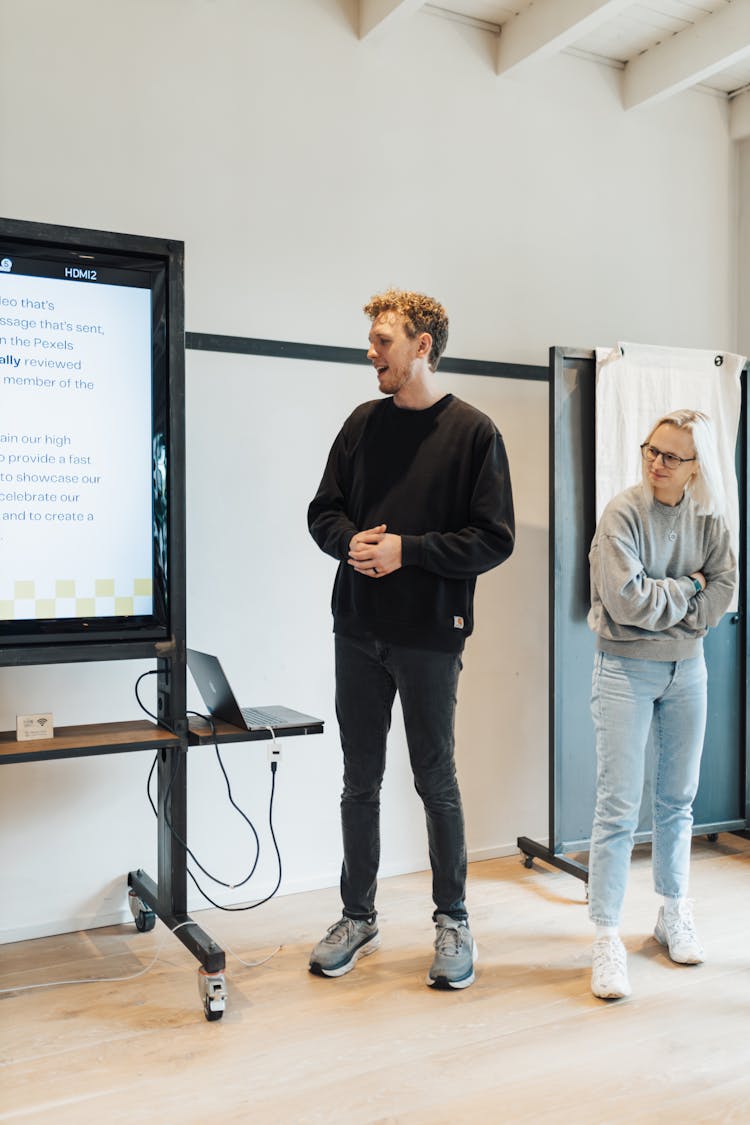 Man And Woman Standing Next To A Whiteboard During A Presentation 