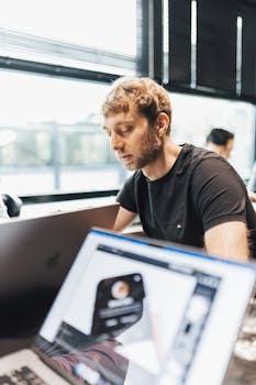 Focused man working with a laptop in a modern office setting, showcasing technology and productivity.