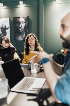 Professionals discussing projects around a conference table with laptops and notepads in an office.