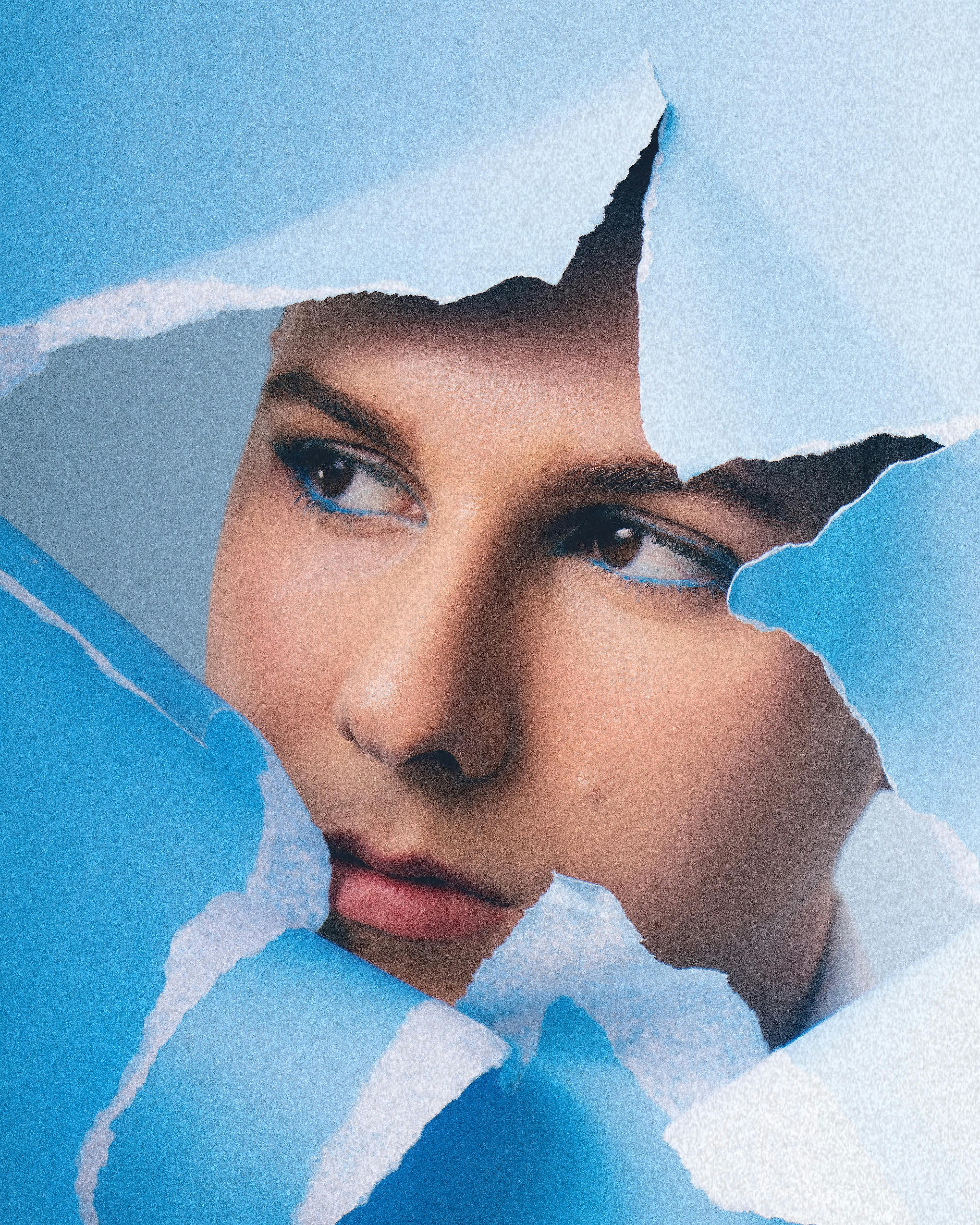 Artistic portrait of a person looking through torn blue paper for a unique visual effect.