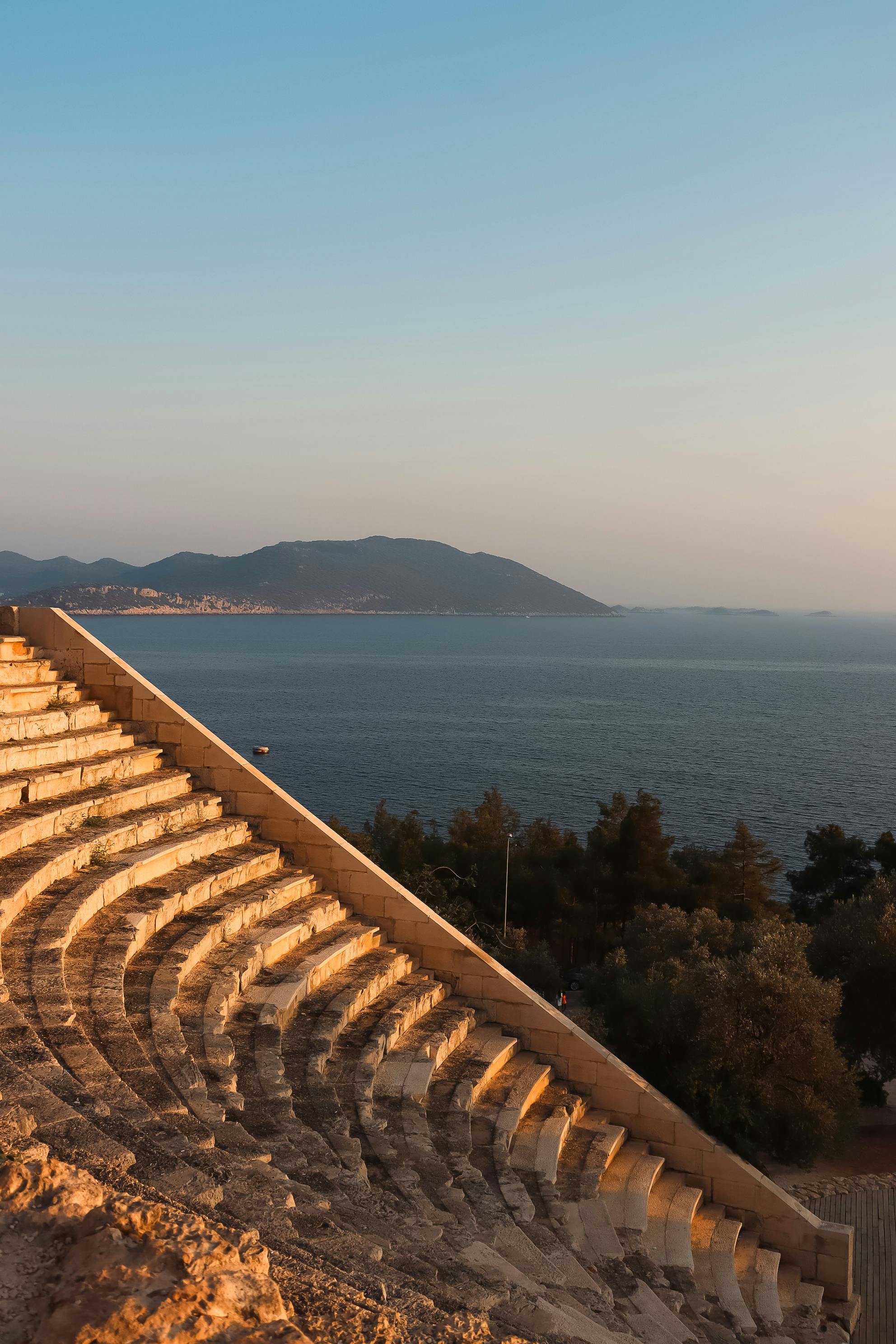 Serene view of an ancient amphitheater with coastal scenery at sunset, showcasing historical architecture.