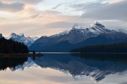 A breathtaking view of snow-capped mountains reflecting in Maligne Lake during a serene day in Jasper National Park.