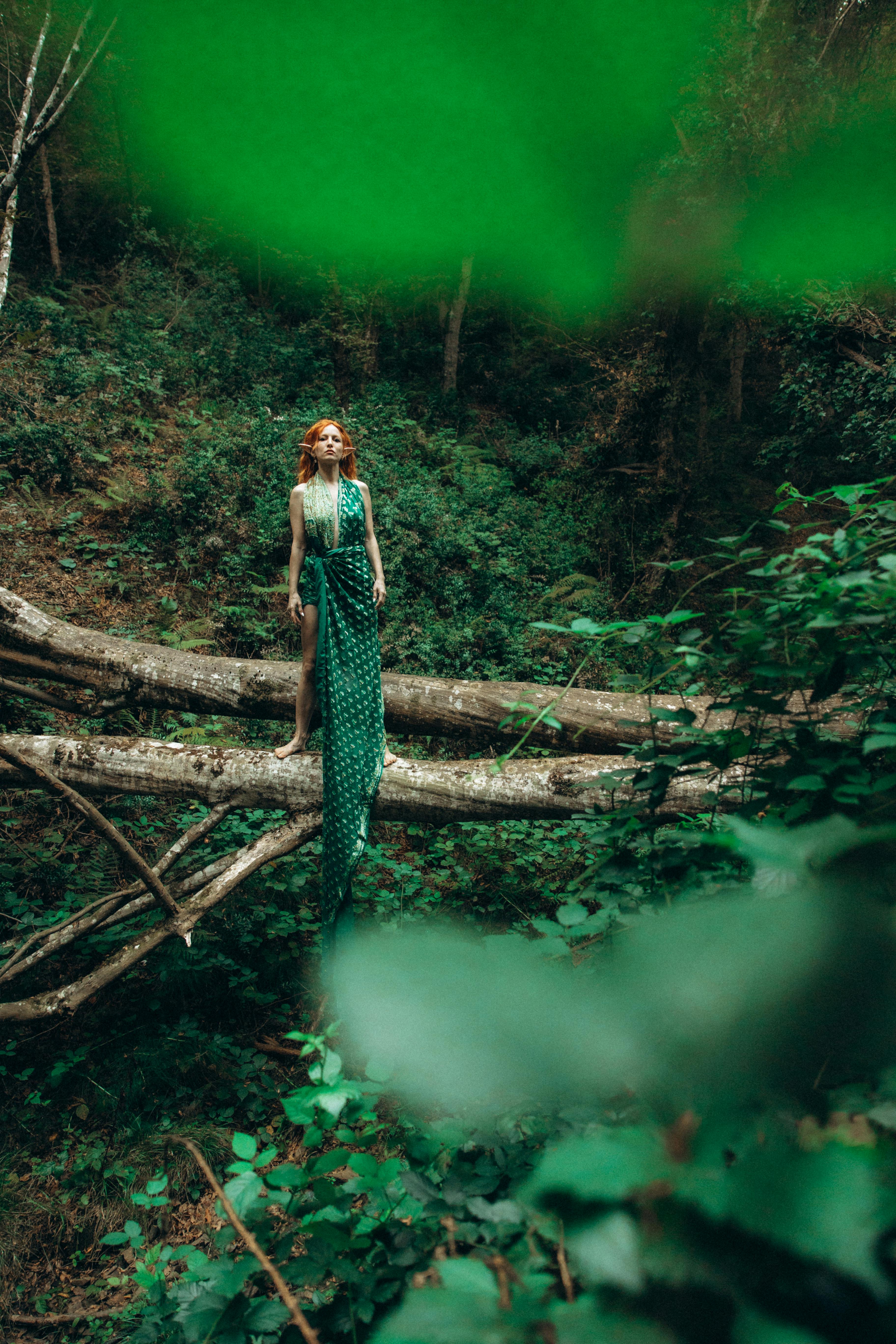 a woman in a green dress standing on a fallen tree