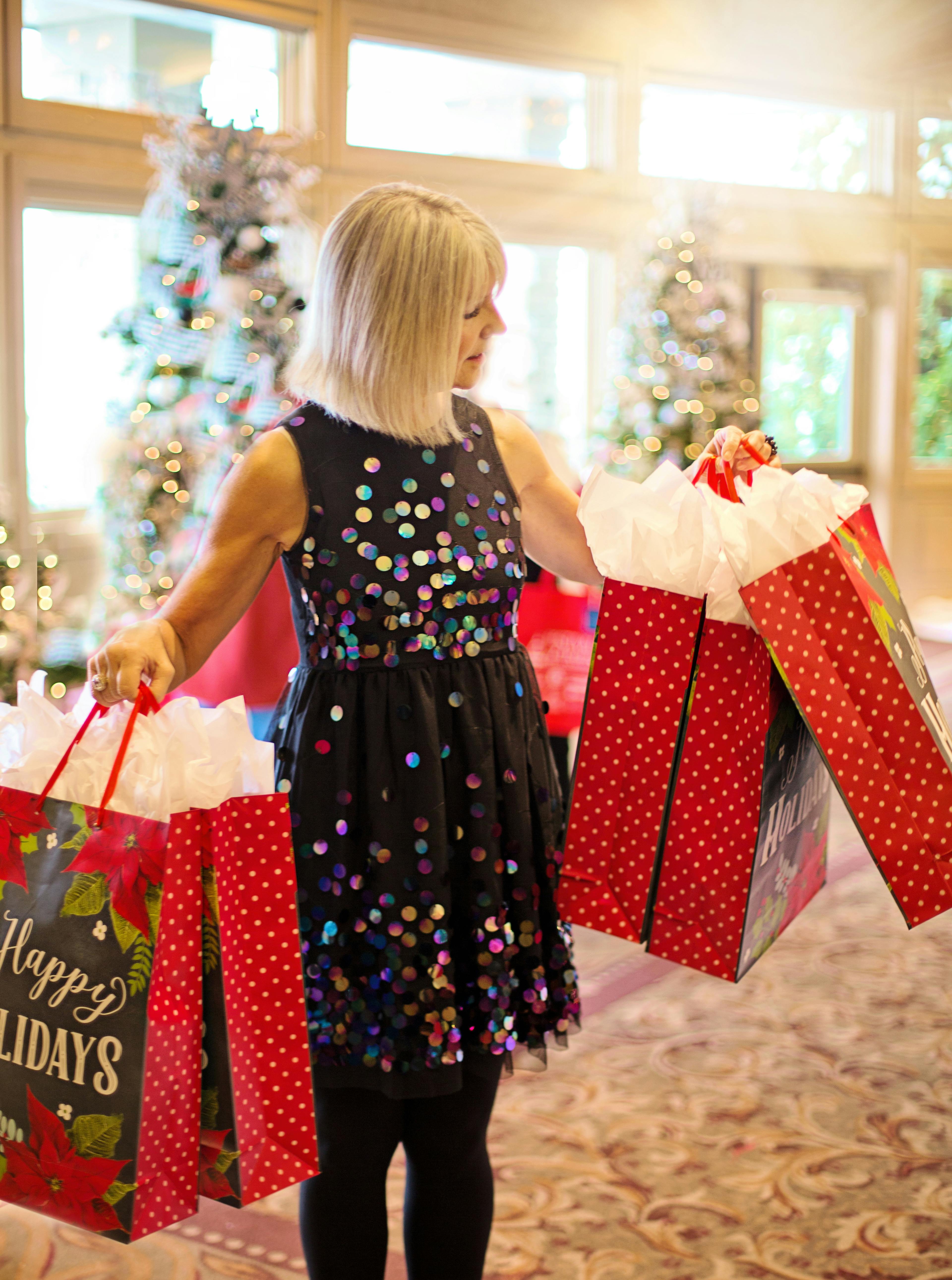 Woman enjoying holiday shopping indoors with colorful gift bags and Christmas trees.