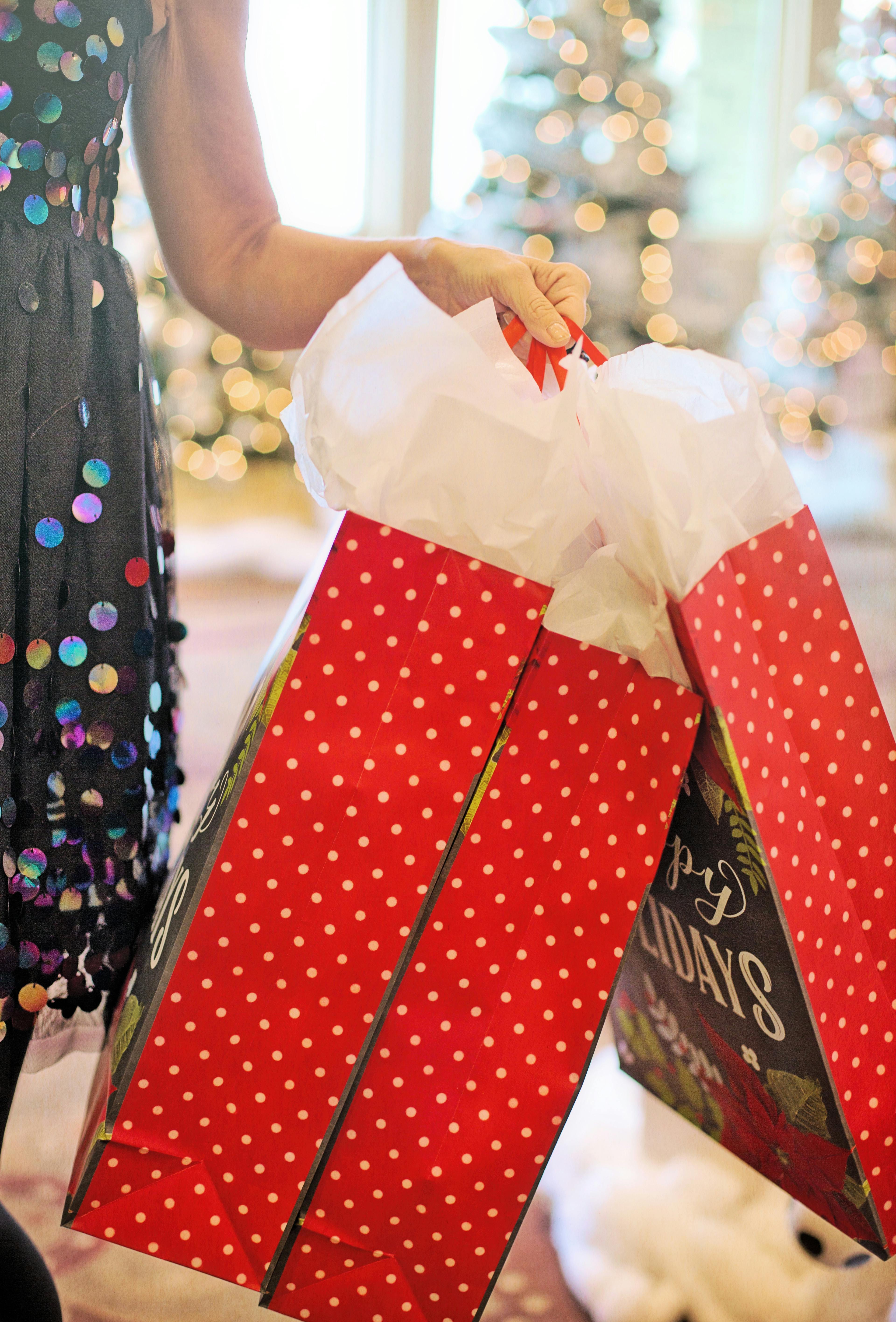 Woman holding Christmas gift bags in festive indoor setting, perfect for holiday celebrations.