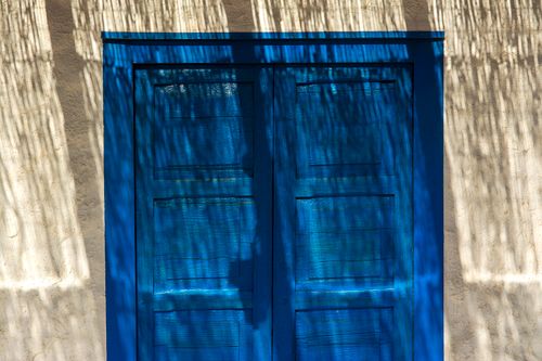 Free Blue wooden door with textured shadows cast by nearby foliage, creating a rustic entrance. Stock Photo
