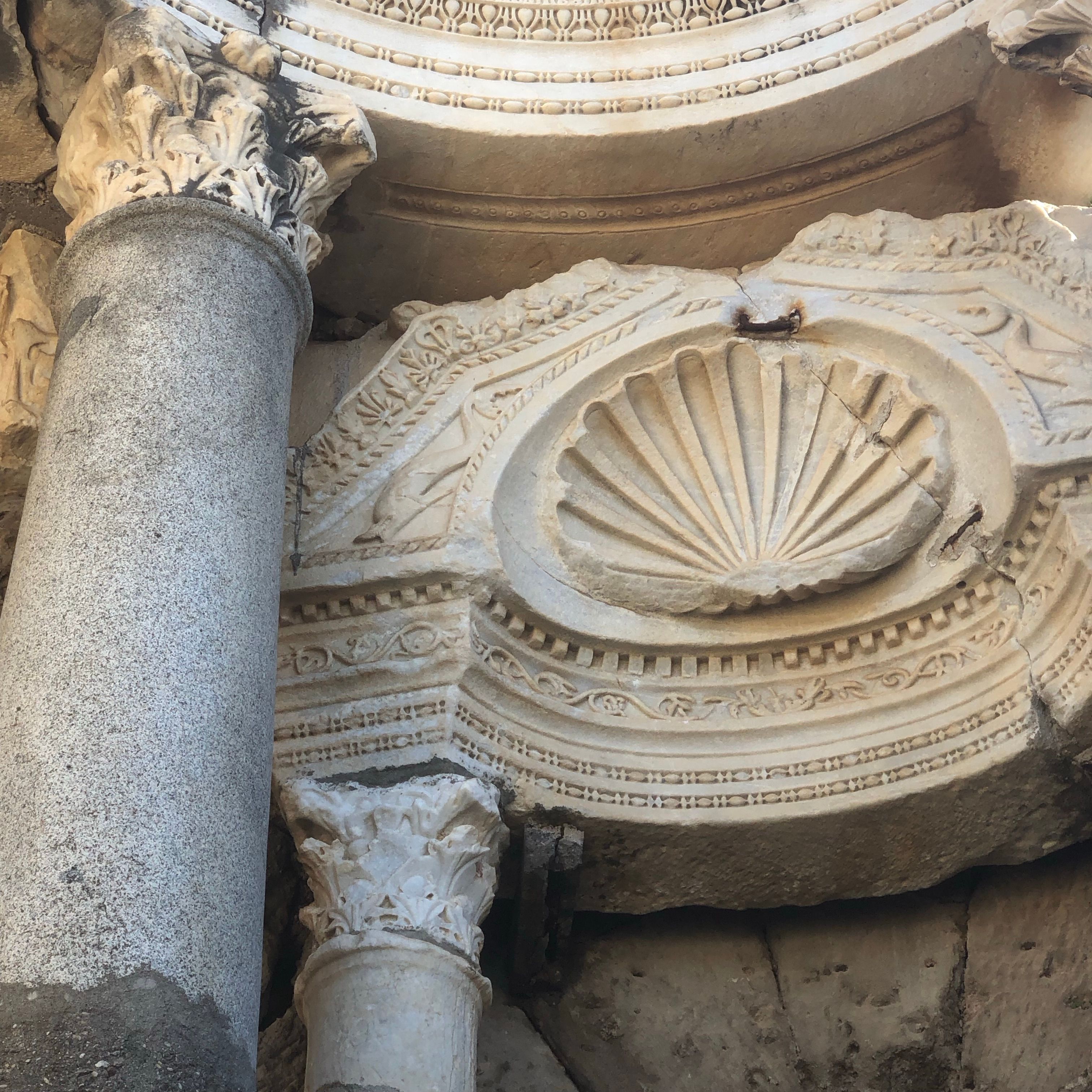 Detailed close-up of an ancient Corinthian column and bas relief with shell design, showcasing intricate marble craftsmanship.