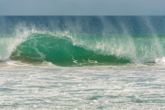 Dynamic ocean wave crashing with foamy splashes under bright daylight, showcasing natural beauty.