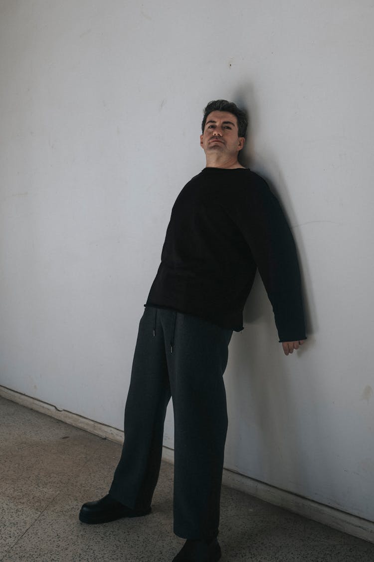 Man In Black Clothes Leaning On White Wall