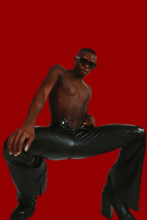 Free Stylish shirtless model in black leather pants against a striking red background. Stock Photo