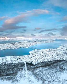 从空中俯瞰，一座白雪皑皑的小镇宁静地坐落在冬日河边，景象令人惊叹