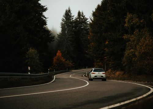 Free A silver car navigates a winding road through a misty autumn forest, evoking a sense of adventure and travel. Stock Photo