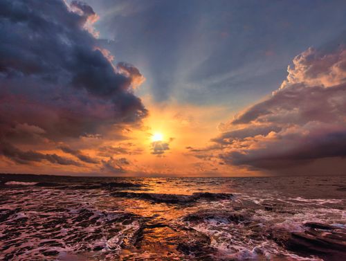 Free Stunning ocean sunset with vibrant clouds and waves crashing on the shore. Stock Photo