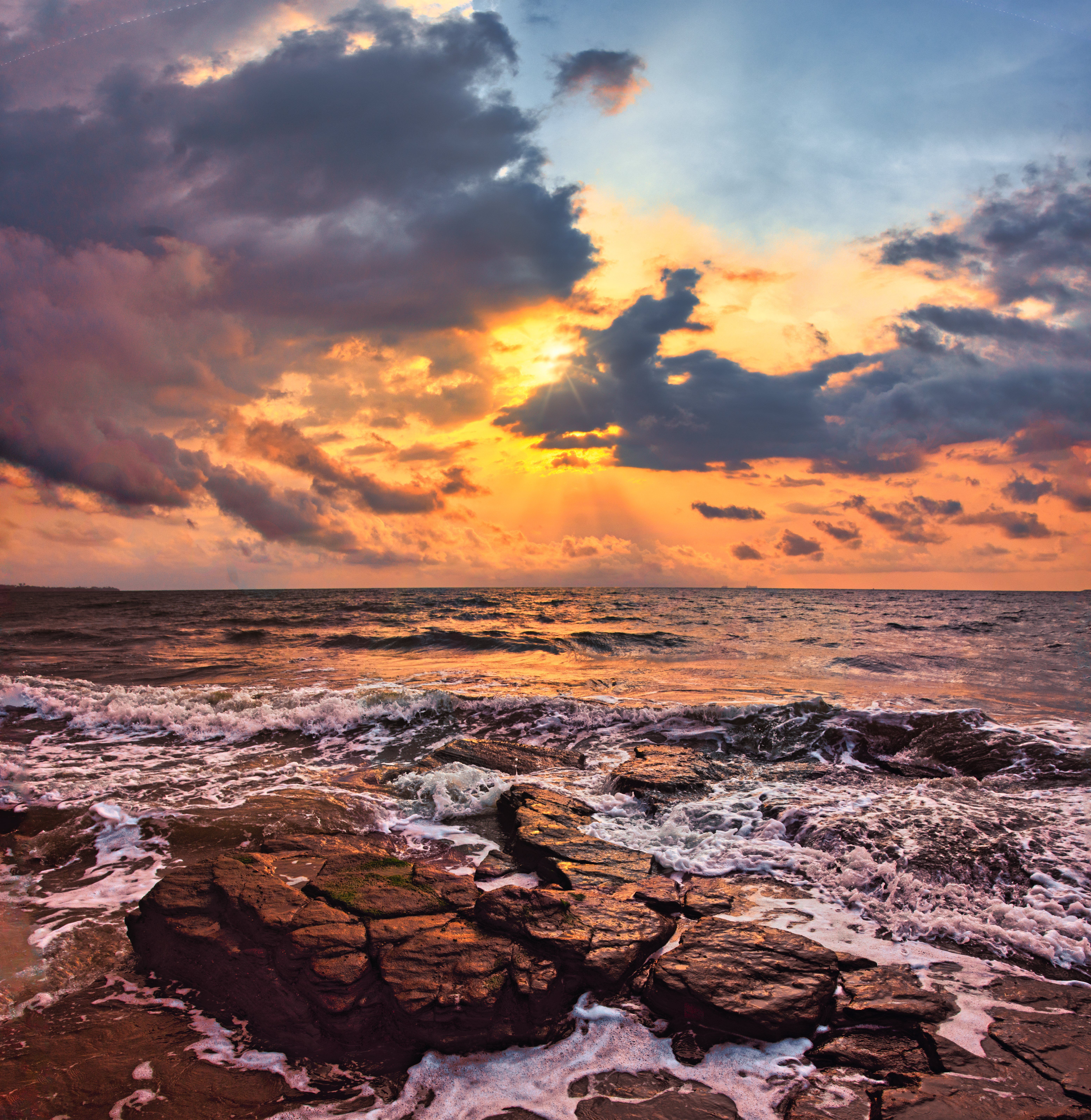 Stunning sunset over ocean with dramatic clouds and eroded shoreline rocks.