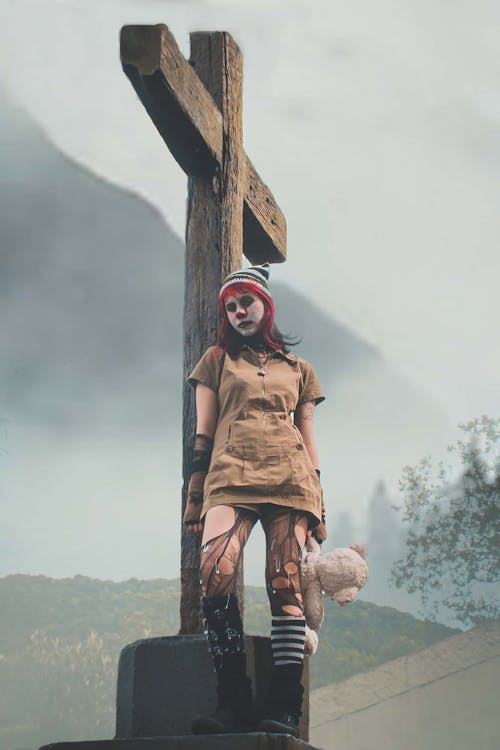 Woman in Ripped Thighs Holding Teddy Bear Standing under Wooden Cross