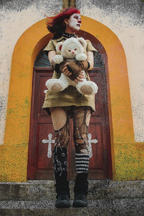Woman with Painted Face and in Torn Tights Standing and Holding Teddy Toy