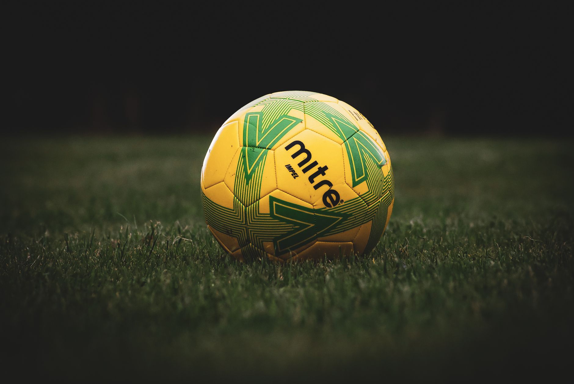 Vibrant yellow soccer ball with green pattern resting on a grassy field, sporty feel.