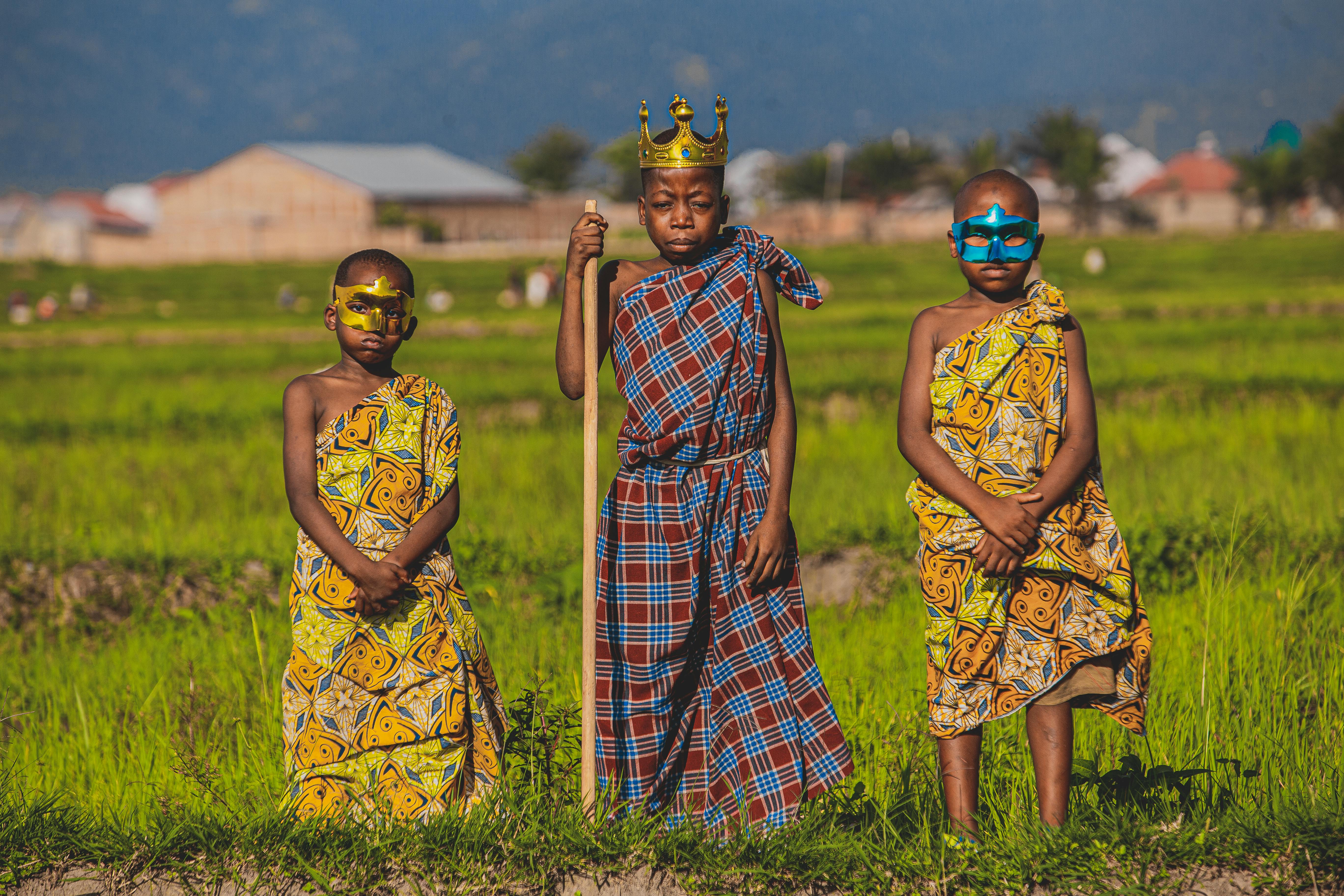 children in colorful patterned tunics wearing crown and face masks