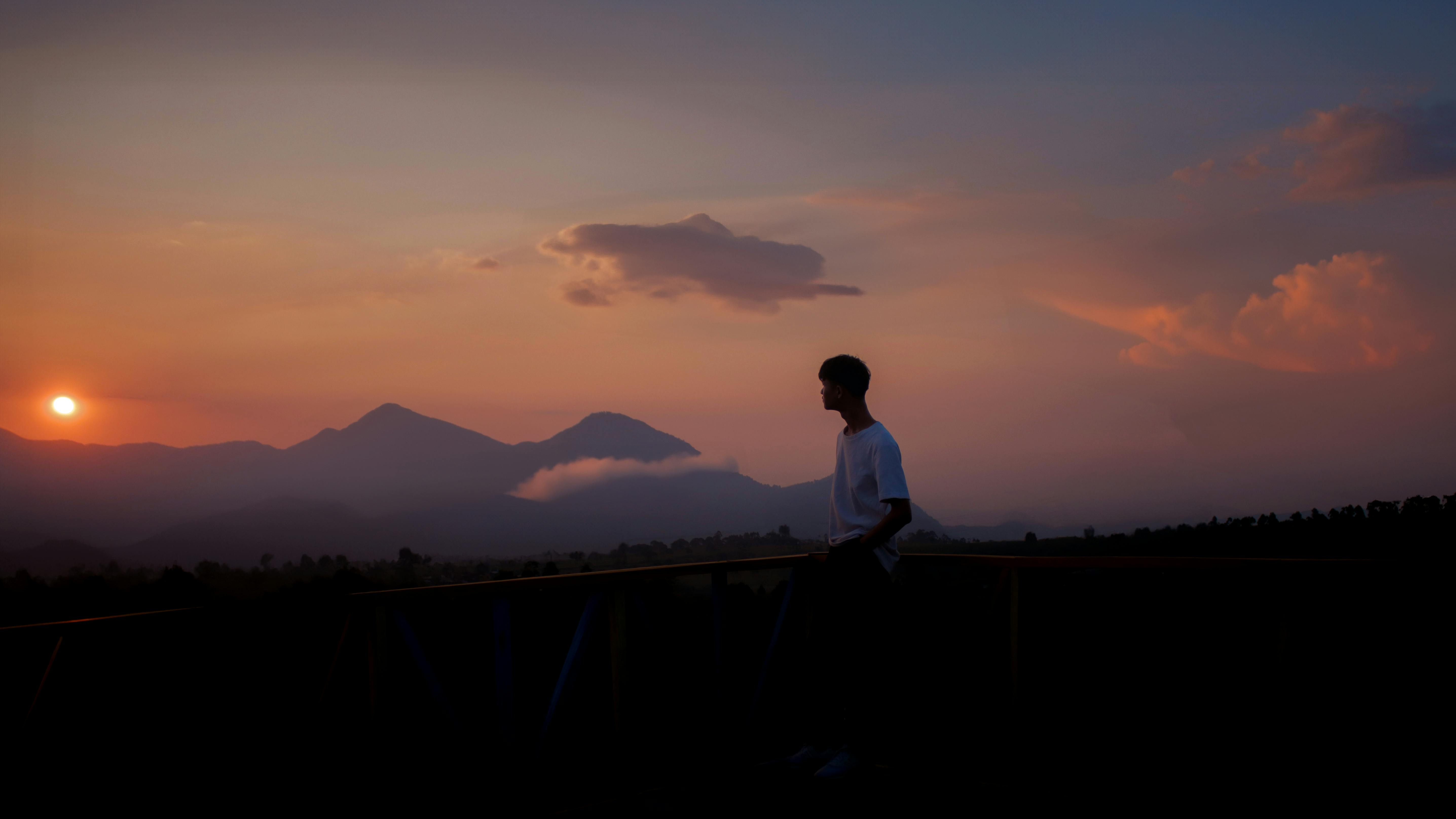 Silhouette of a man standing against a beautiful sunset over mountains. Peaceful and serene scenery.