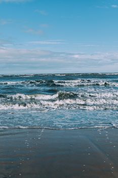 Peaceful scene of ocean waves gently rolling onto a sandy beach under clear blue skies.