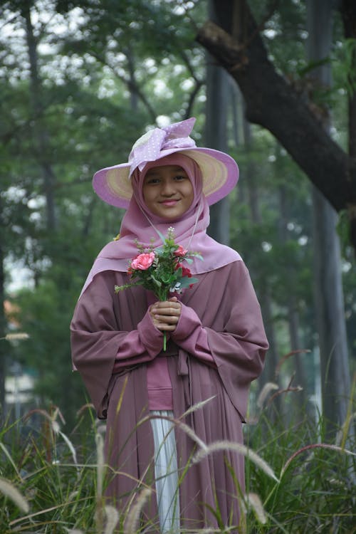 Smiling Woman in Pink Hat and Hijab Standing with Flowers