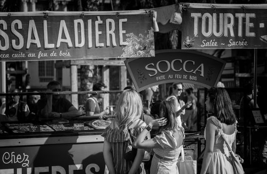 A bustling street market scene in Nice, France, featuring people browsing food stalls.