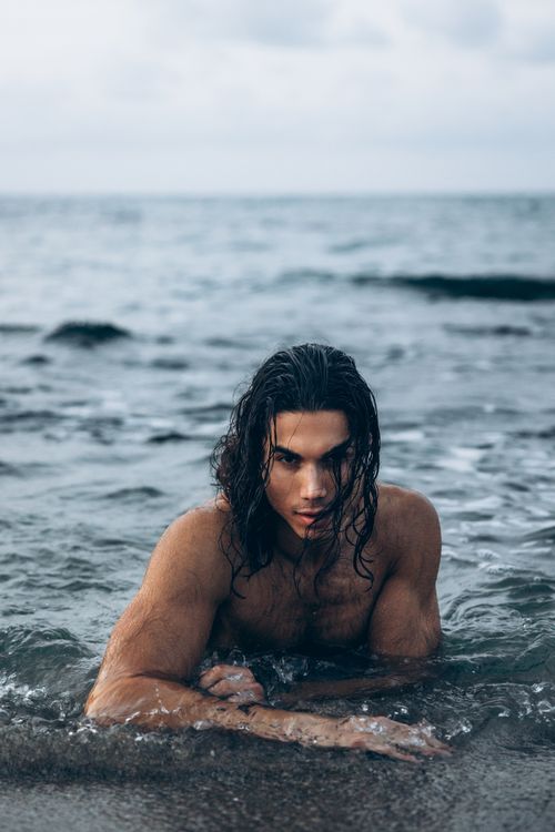 Free A man with long hair poses in ocean waves at a beach during daytime, evoking a sense of adventure and relaxation. Stock Photo