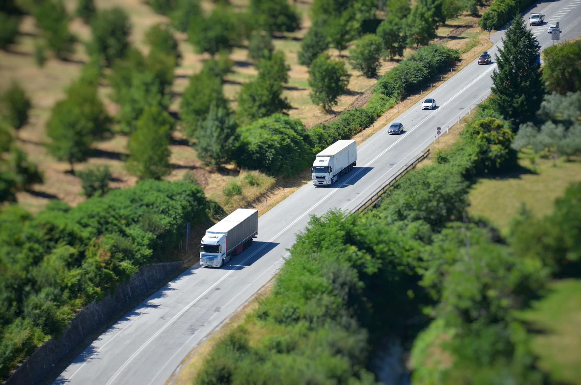 Aerial shot of a highway with trucks and cars surrounded by lush greenery.