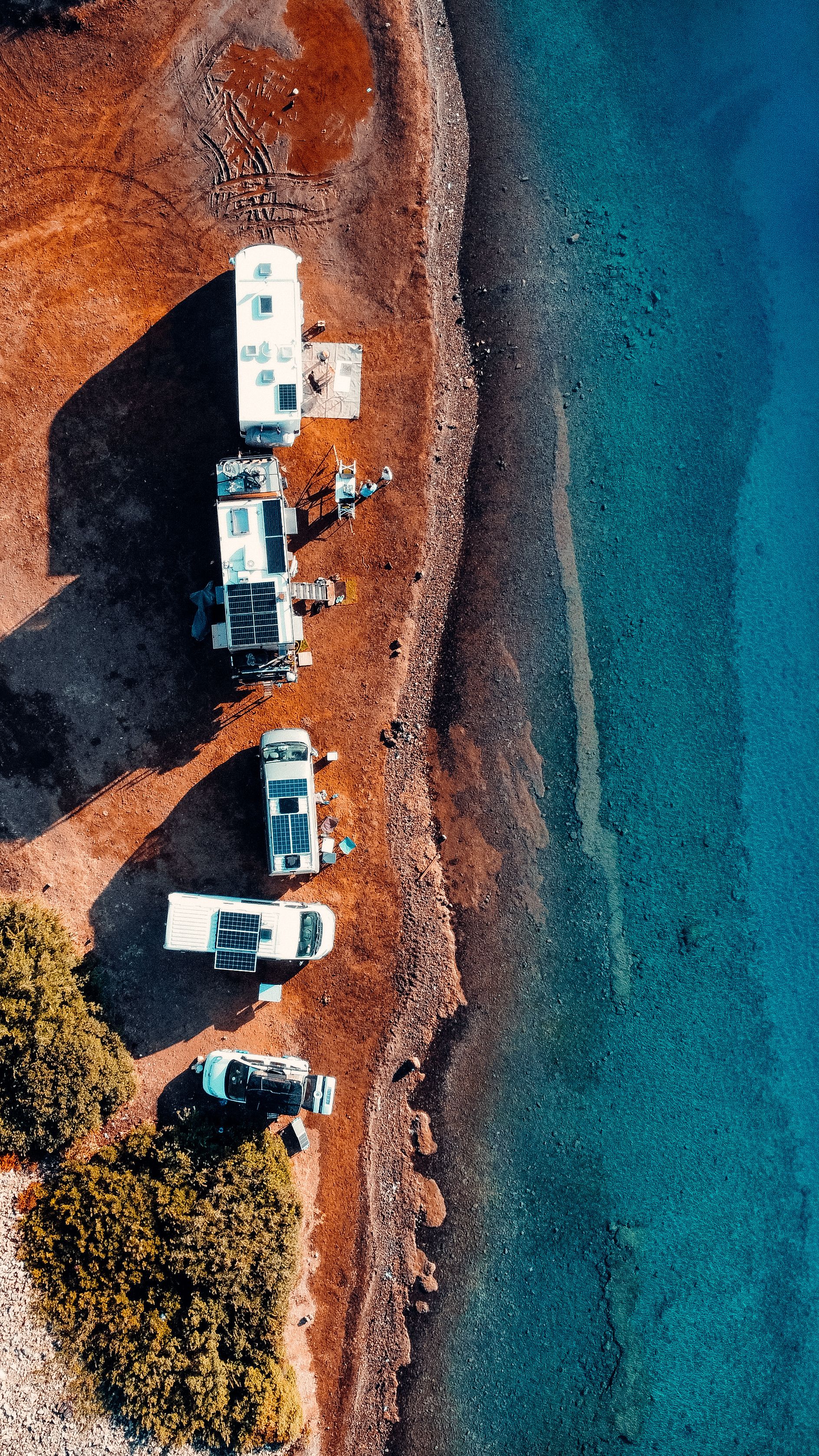 Aerial view of recreational vehicles parked on a shoreline, each fitted with roof solar panels charging a 24V battery bank