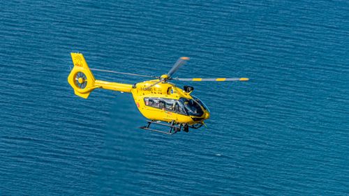 Free A bright yellow rescue helicopter flying over clear blue ocean waters, capturing an aerial view. Stock Photo